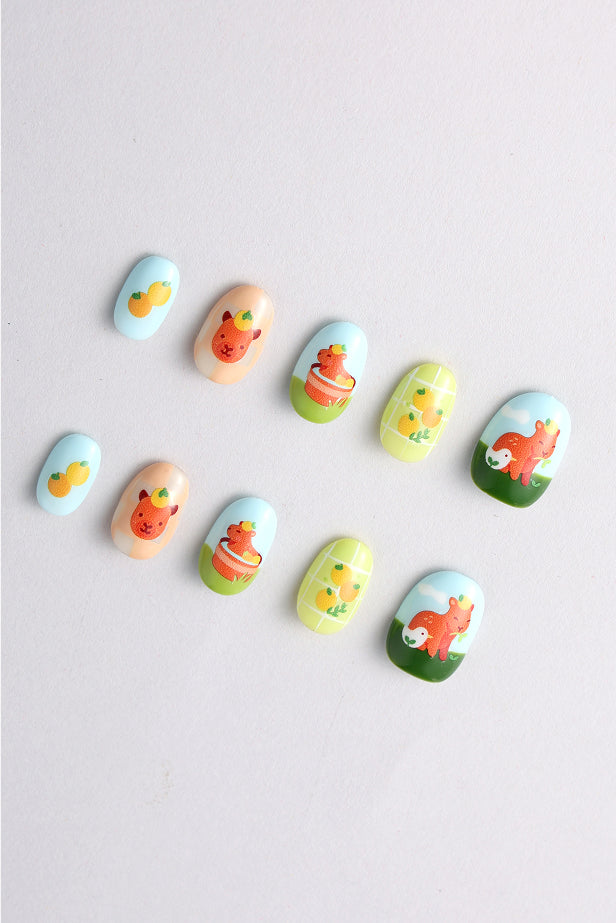 Press-on nails with cute capybara art by Alice Lee. Features peach, blue, green nails with capybaras and fruit.