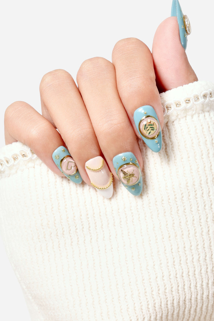 Light blue press-on nails with gold accents, featuring a heart and bee charm.