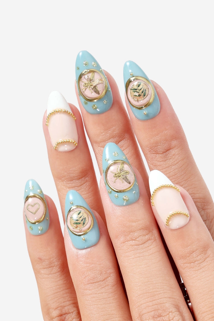 A Touch of Charm press-on nails with blue, gold, and pastel accents, featuring bee and leaf charms.