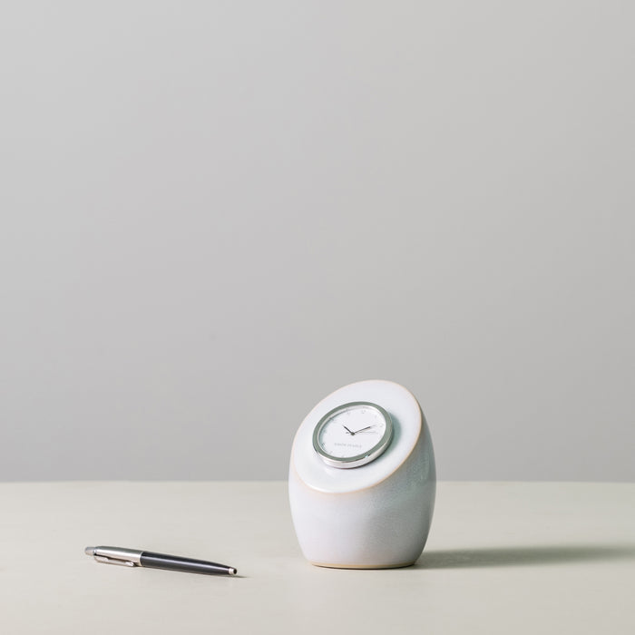 White ceramic rounded clock with gray trim and white dial face, displayed next to a pen for scale.