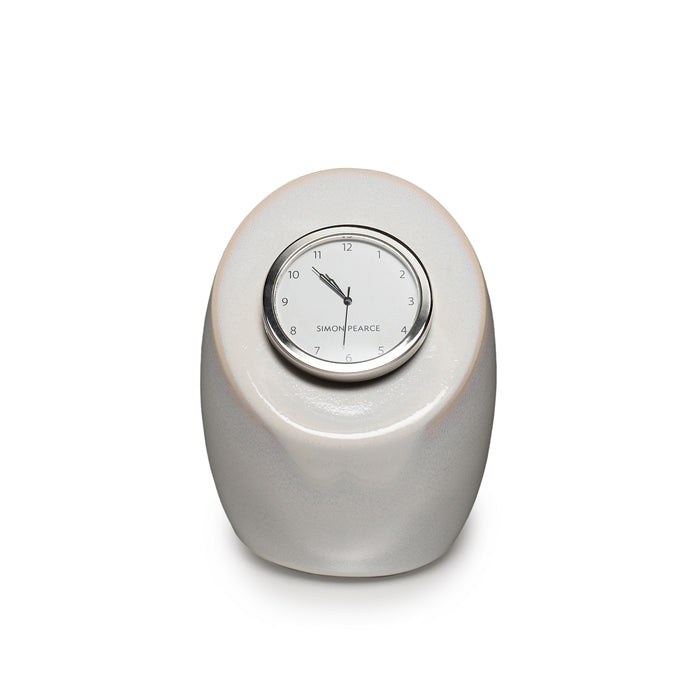 Cream pottery clock with rounded oval base and circular dial marked with Simon Pearce branding.