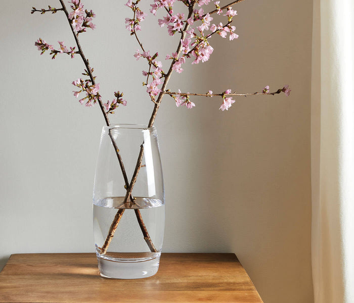 Clear glass vase with two branches of pink cherry blossoms and water inside.
