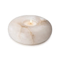 White alabaster tealight holder with lit candle and natural veining throughout.