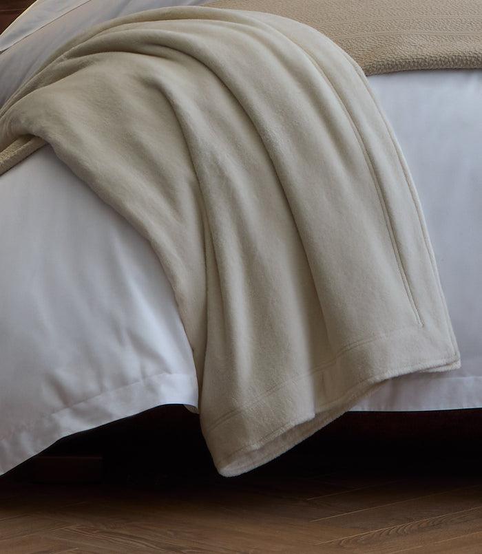 All Seasons Cotton Blanket laid over the corner of a white bed