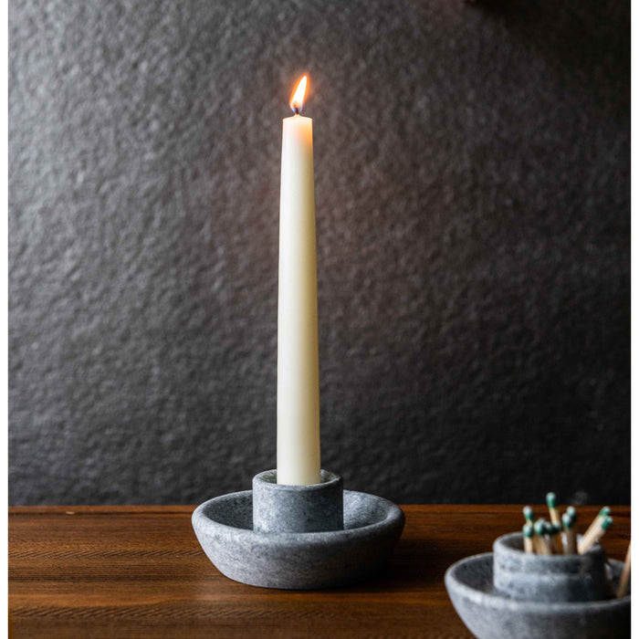 Gray soapstone taper candle holder with lit cream-colored candle on wooden surface.