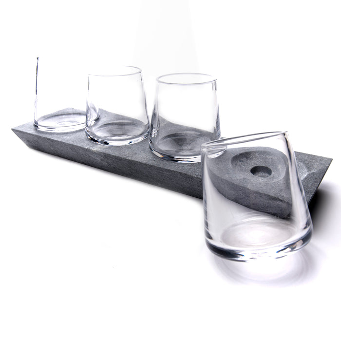 Four clear whiskey glasses arranged on a gray soapstone base with circular indentations.