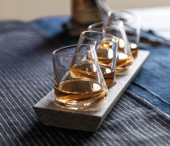 Four whiskey glasses filled with amber liquid seated on a gray soapstone base.