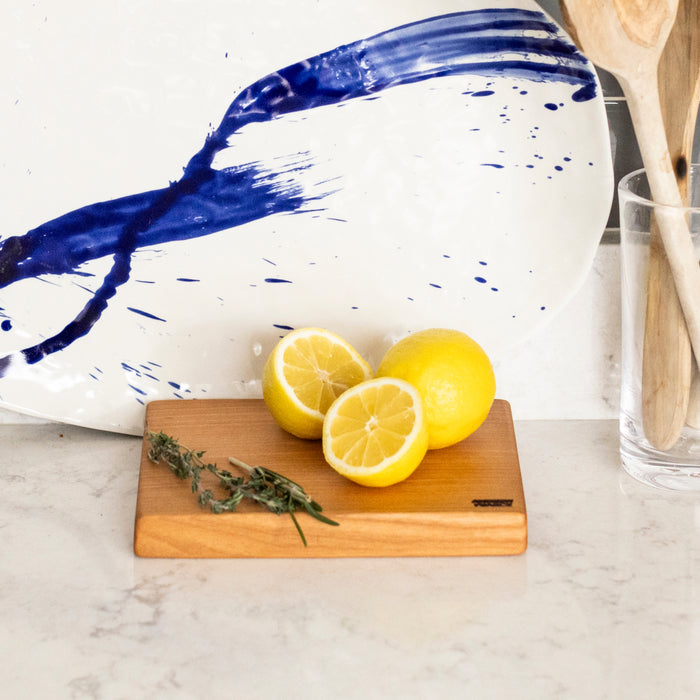 Cherry wood cutting board with square edges, holding sliced lemons and fresh thyme sprigs.