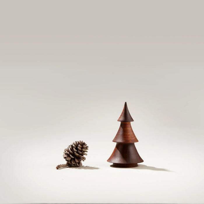 Dark walnut wood evergreen tree sculpture with stacked conical sections next to a pinecone.