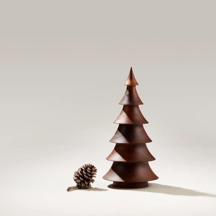 Stacked walnut wood evergreen tree with pointed top and tiered cone sections, displayed with a small pinecone beside it.