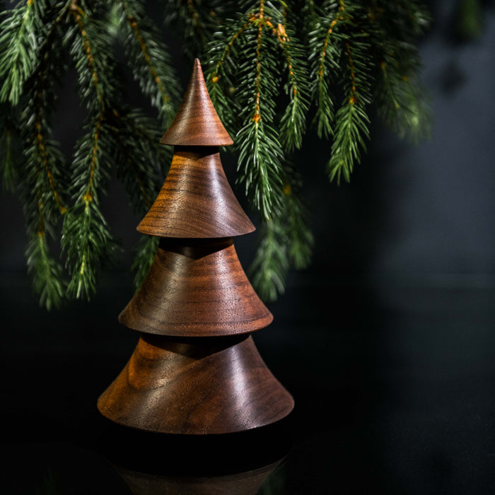 Stacked walnut wood tree-shaped ornament with pointed top beneath evergreen branches.