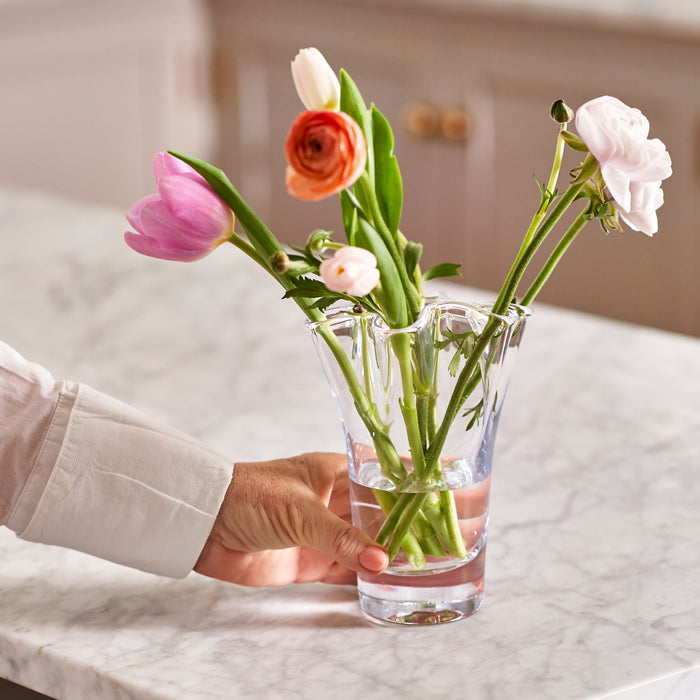 Clear glass vase holding pink, red, and white flowers with green stems in water.