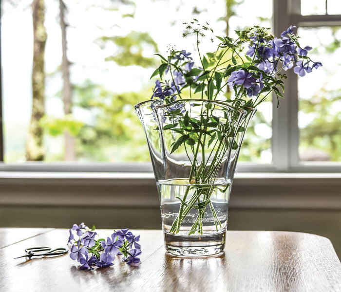 Clear glass vase with vertical ribbed pattern holding purple anemone flowers and green stems with water inside.
