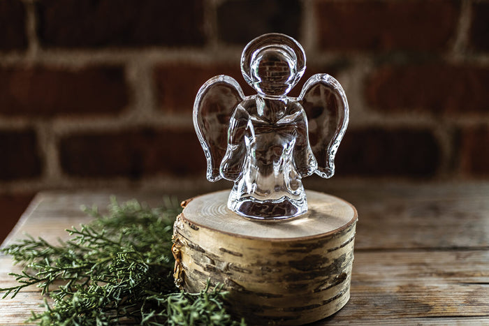 Clear glass angel figurine with wings and halo sitting on wooden base with greenery.