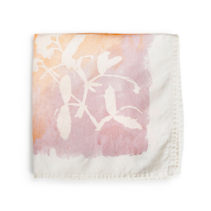 Apricot linen napkin with white botanical leaf print fading from peachy-orange to mauve tones.