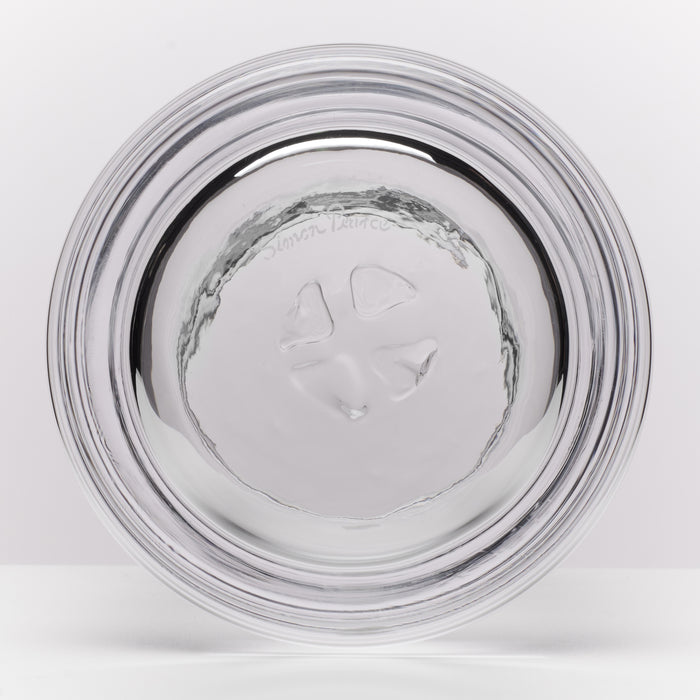 A clear glass with a thick, rounded base and a textured, hammered pattern, shown from the bottom on a light gray background.
