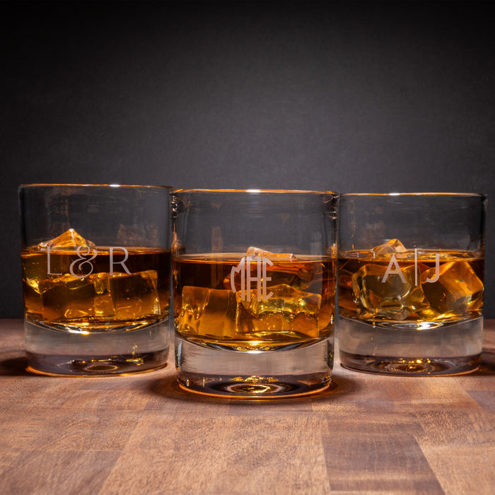Three double old-fashioned glasses filled with amber liquid and ice cubes, each etched with initials.