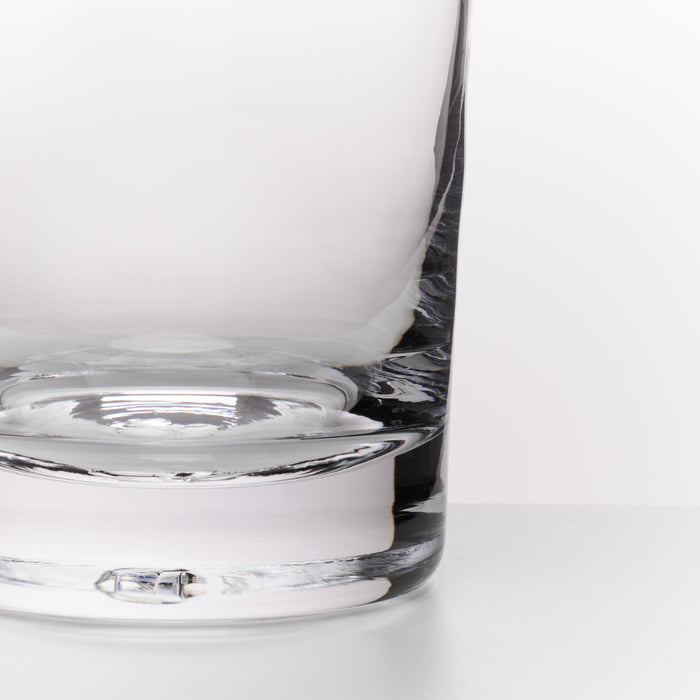 Close-up of a clear glass tumbler with a thick, rounded base on a clean white surface.