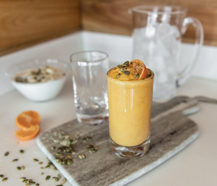 Two clear highball glasses with one filled with yellow cocktail and orange slice garnish, displayed with pitcher and table se