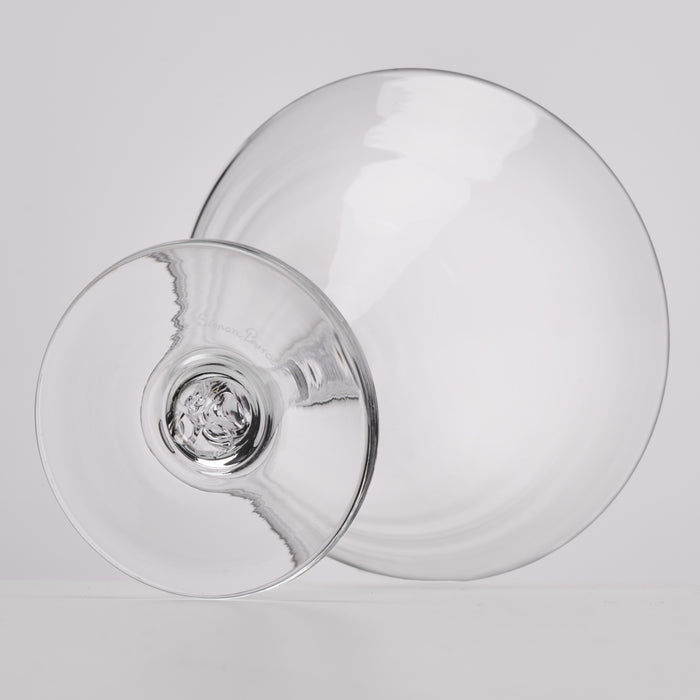 A clear glass stemmed martini glass or cocktail glass shown from an angled top-down view on a light gray studio background.