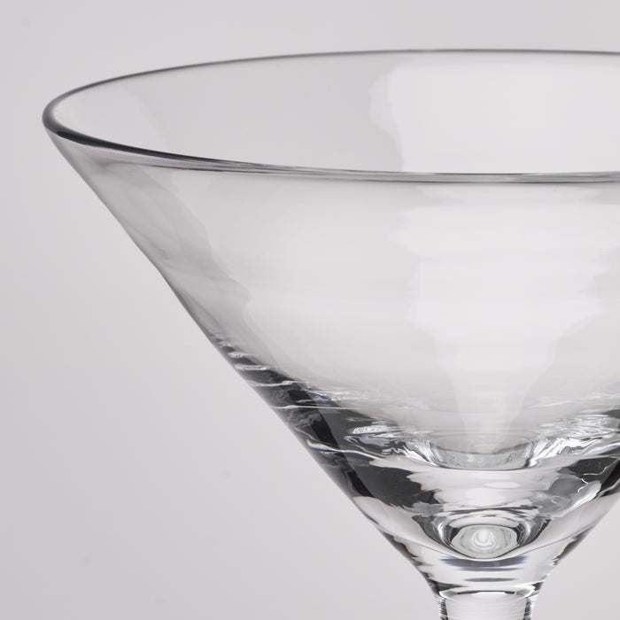 A close-up of a clear glass martini glass on a light gray background.