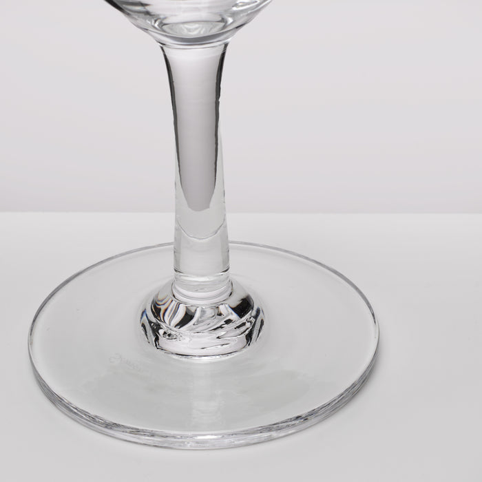 A close-up of a clear glass wine glass showing the stem and circular base against a light gray background.