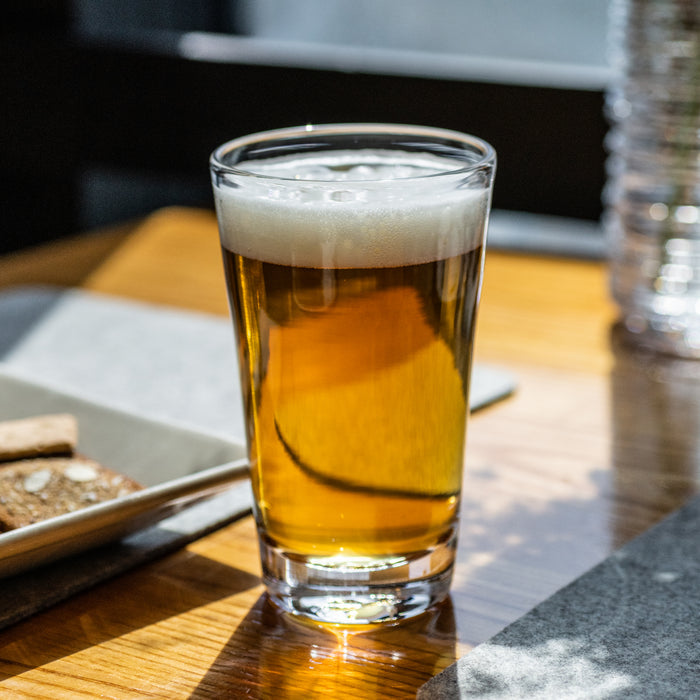 Clear pint glass filled with amber beer and white foam head, sitting on wooden surface.