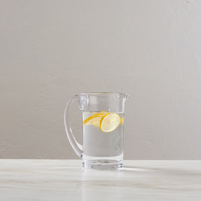 Clear glass pitcher filled with water and lemon slices on a white surface.