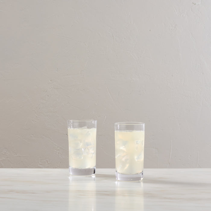 Two clear glass tumblers with white bands containing ice and pale liquid on white surface.