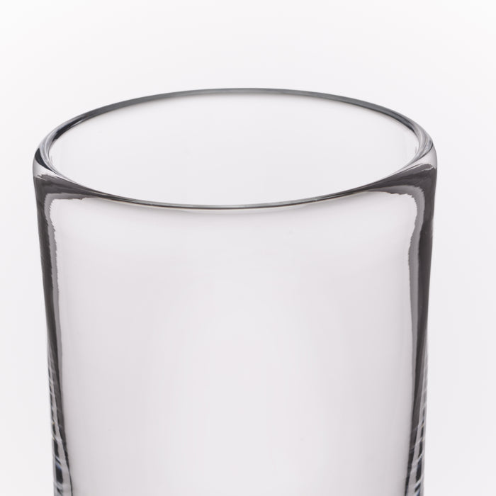 A close-up of a clear glass tumbler with a thick, rounded rim and subtle vertical textured detailing near the base, shown against a plain white background.