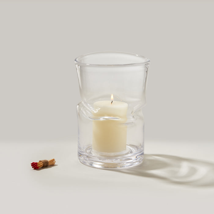 Large clear glass hurricane with cream-colored pillar candle inside and bundled matches beside it.