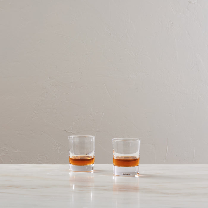 Two clear whiskey glasses filled with amber liquid, placed side by side on a white surface.