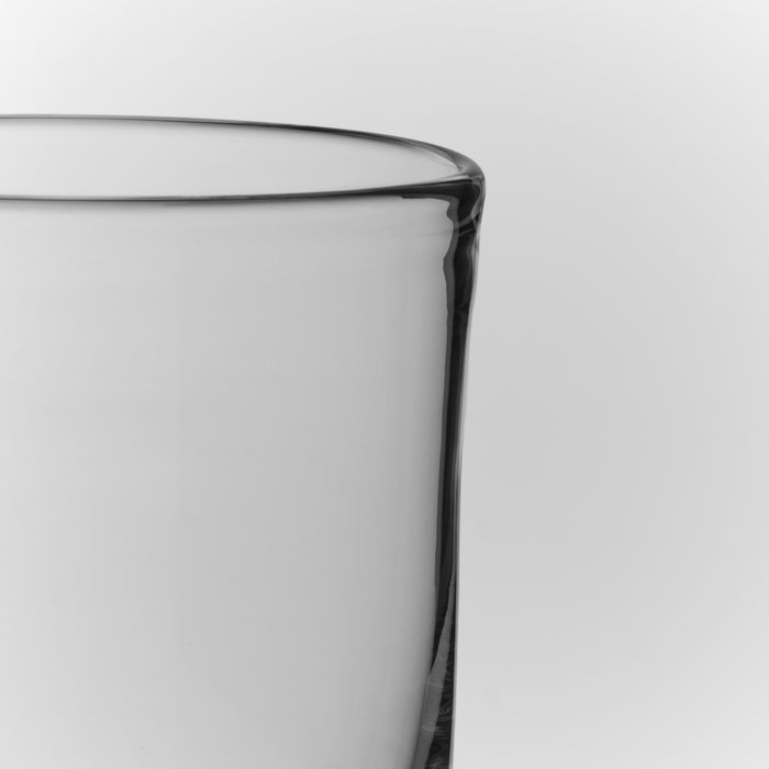 Clear glass tumbler with straight sides and a rounded rim, shown from a close angle against a light background.