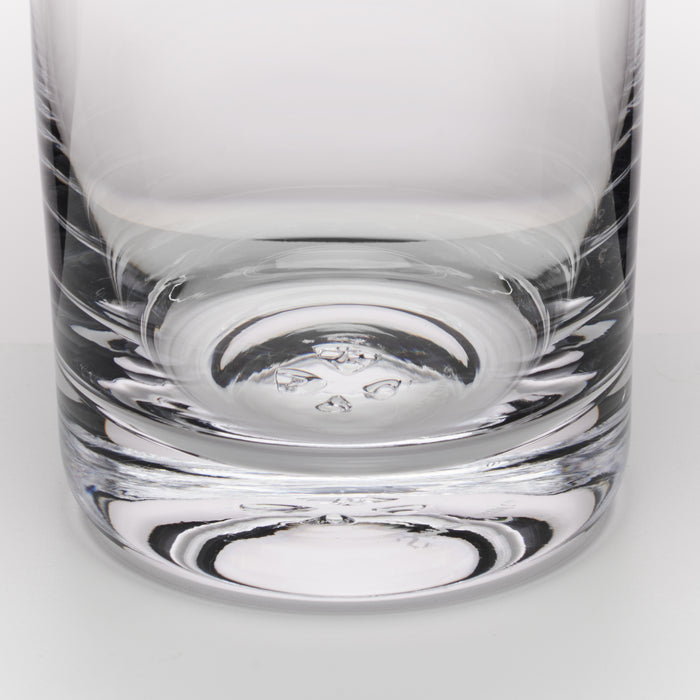 A close-up of a clear glass tumbler with a thick, textured base, showing reflections on a light gray background.