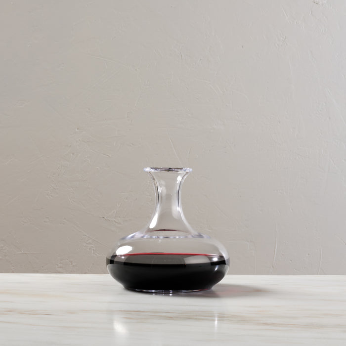 Clear glass wine decanter with wide bulbous base and narrow neck, containing dark red wine.