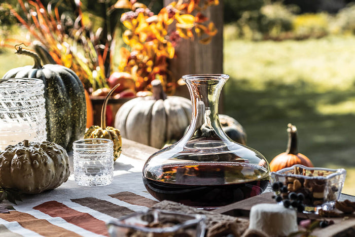 Clear glass wine decanter with wide base and narrow neck, filled with red wine, displayed on outdoor table with autumn décor.
