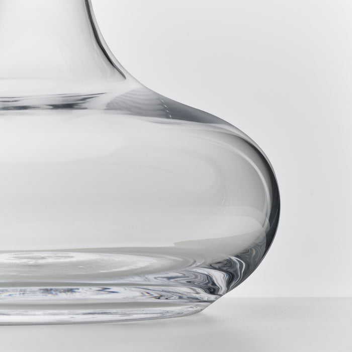 Clear glass wine decanter with curved sides and wide base, shown in close-up detail.