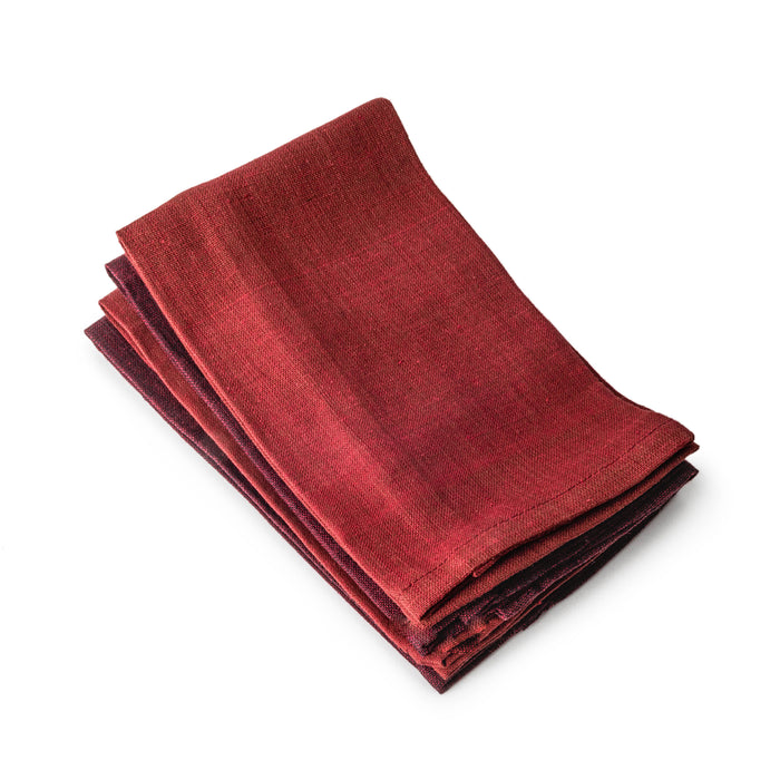 Four folded auburn-red linen napkins stacked together with visible texture.
