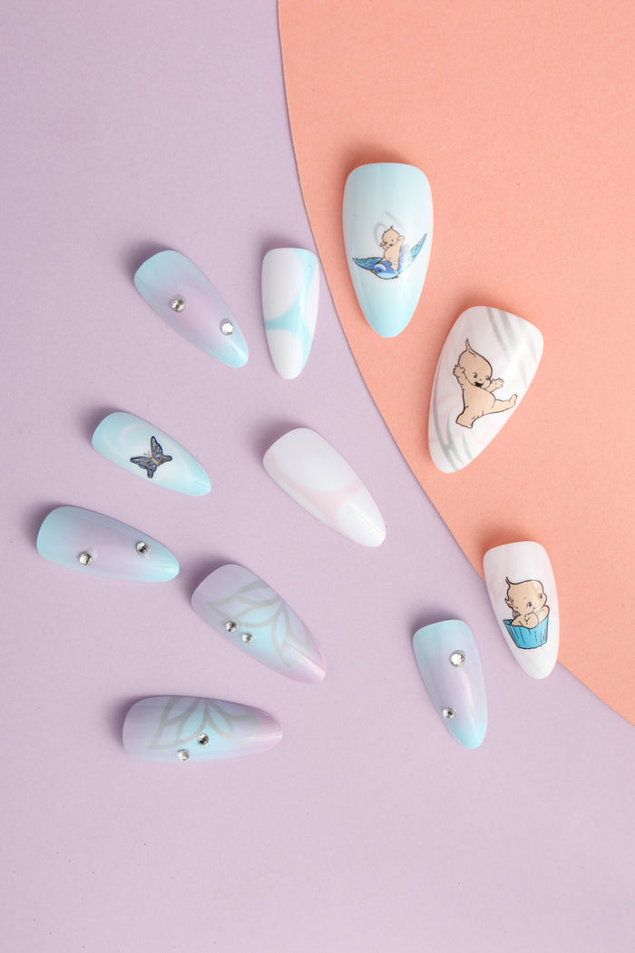 Aura Kewpie press-on nails with playful designs, including a baby on a bird and in a cupcake.