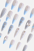 Baby blue and white press-on nails with bow accents and rhinestones.