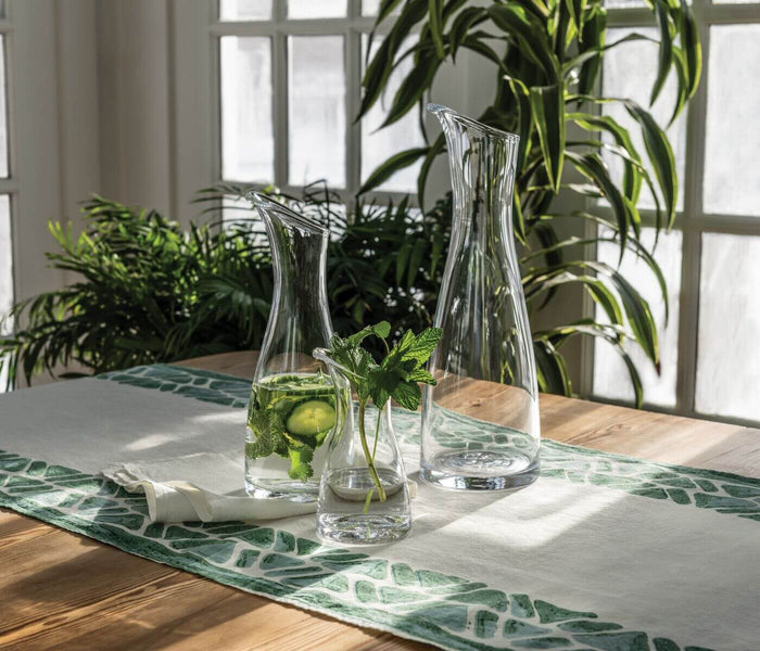 Clear glass carafe with vertical ribbed texture, displayed on wooden table with beverage and fresh mint.