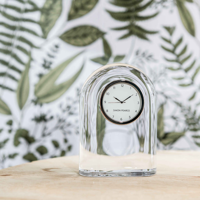 Clear glass dome-shaped clock with rounded arch top and Simon Pearce branding on white dial.