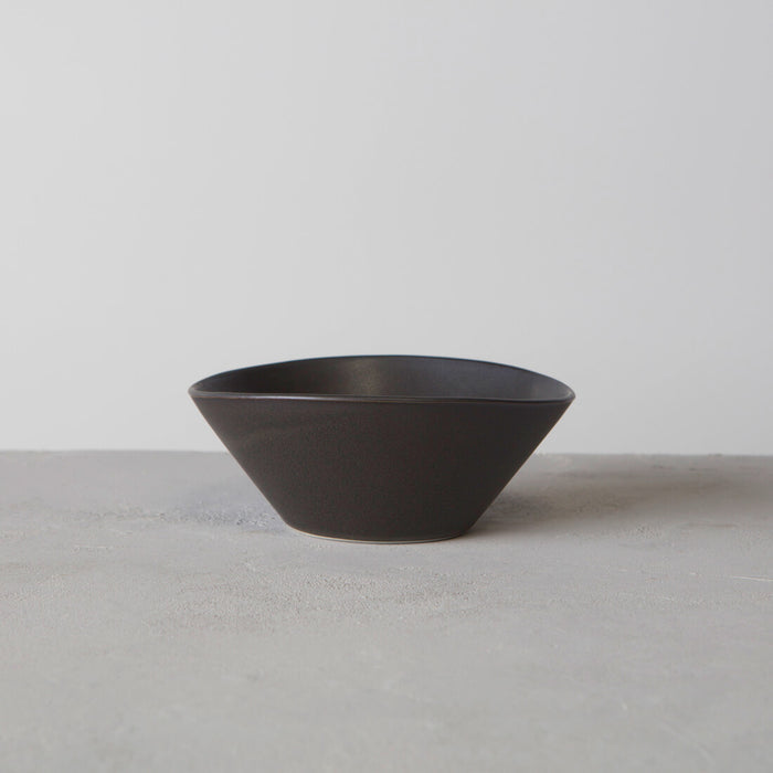 Dark slate-colored ceramic bowl with tapered sides and wide opening on neutral surface.