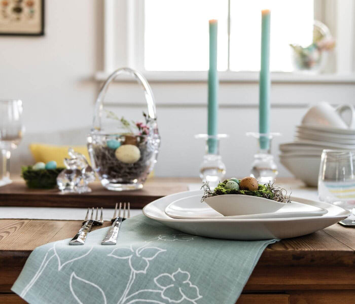 White ceramic bowl nested on stacked white plates, filled with moss and decorative eggs, displayed on a formal dining table s