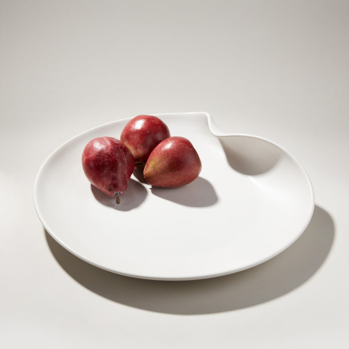 White ceramic platter with curved edge and three red pears on surface.