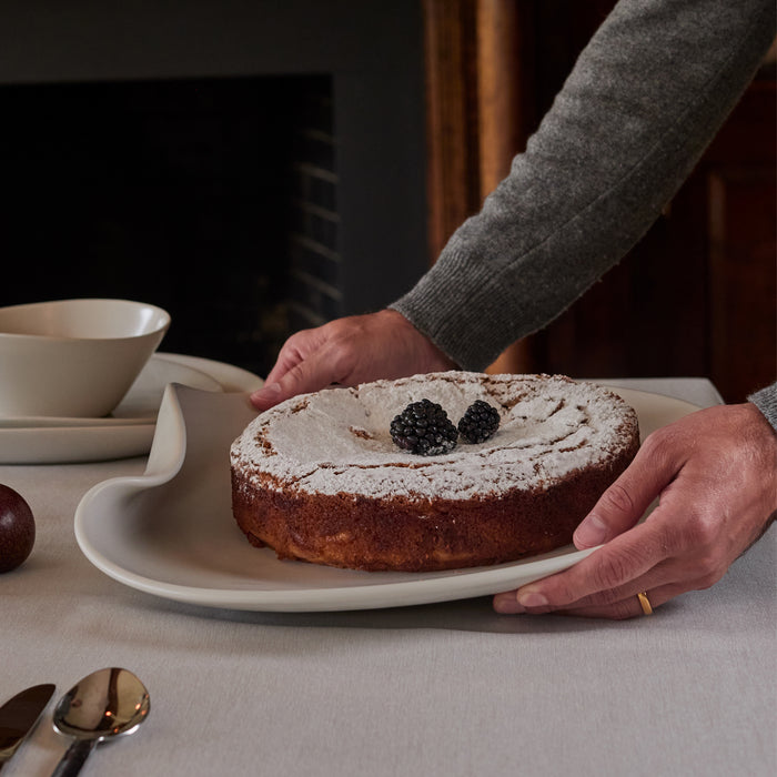 Round cake with powdered sugar dusting and fresh blackberries on top, displayed on a white plate.