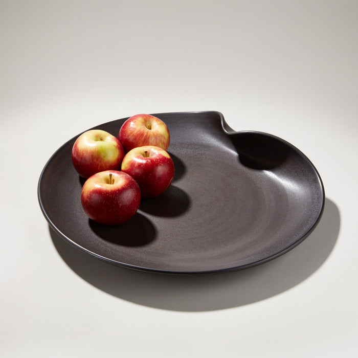 Black organic platter with wavy edges holding four red apples.