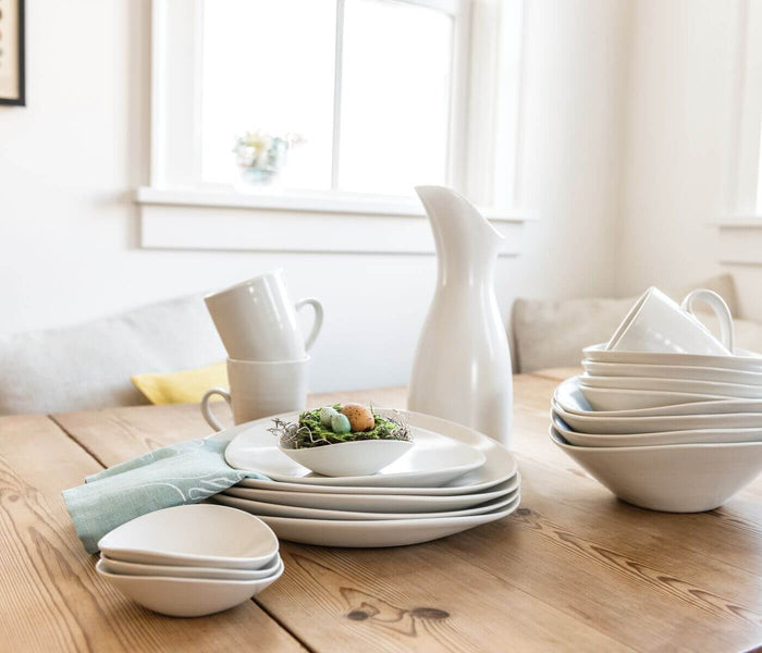 White ceramic serving bowl with curved sides displayed on wooden table among matching dinnerware.