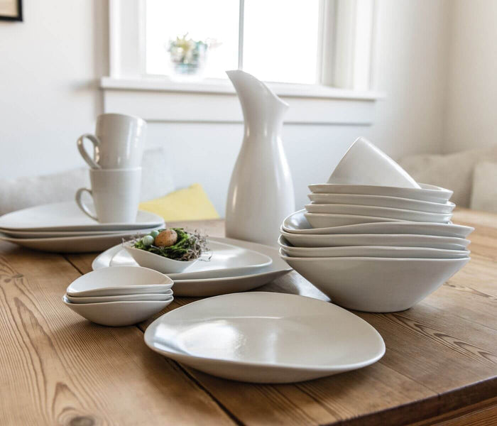 White ceramic serving bowl with curved sides displayed on wooden table among matching dinnerware.