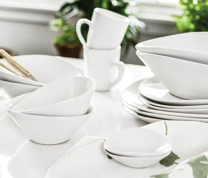 White oval ceramic side plate with curved edges displayed among coordinating dinnerware.
